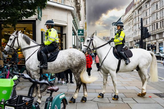 Two police officers on white horses patrol the street near parked bicycles.